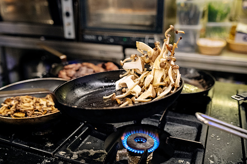 Side on view as a chef  cooks a selectionof pan fried mushrooms, enoki, portobello and oyster mushrooms, in a frying pan. Colour horizontal with some copy space.