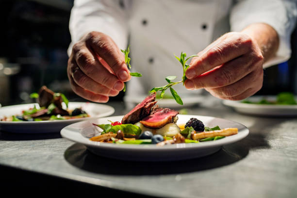 Pan fried duck. Chef adding the final flourish by adding some liquorice flavoured  parsley to the dish. The dish is, pan fried pink duck breast onto a bed of parsnip puree with seasonal autumn vegetables and berries. Colour, horizontal with some copy space, photographed on location in a restaurant on the island of Møn in Denmark. food and drink stock pictures, royalty-free photos & images