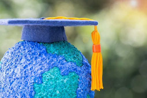 Education world or Graduated study abroad international ideas. Graduation hat on top Paper Mache Craft Earth globe. Concept of Congratulations to graduates university lead to success in world amd life