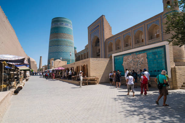 Tourists in front of tourist information map, drawing after entering the Ancient city’s old town of Khiva in Uzbekistan Khiva, Uzbekistan - August 05, 2018: Tourists in front of tourist information map, drawing after entering the Ancient city’s old town of Khiva in Uzbekistan. In background are souvenirs stands in front of highest minaret in Khiva. Oriental buildings of old city on sunny day against clear blue sky. khiva stock pictures, royalty-free photos & images