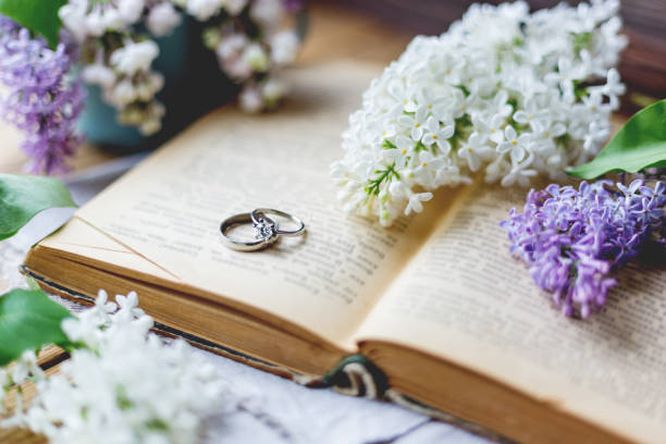 paire de bagues de mariage avec diamants. fond rustique avec vieux livres et fleurs lilas. fond rétro. - jewelry obsolete old gold photos et images de collection