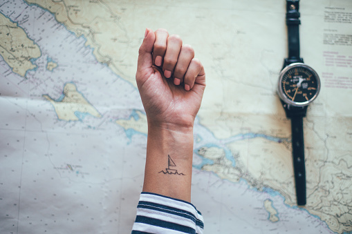 Small ship tattoo on female ankle with nautical map in background . Sailing, travel, adventure, wanderlust, tourist concept.