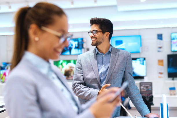 istock Smiling multicultural couple looking for new smart phone. Tech store interior. Selective focus on man. 1081453620