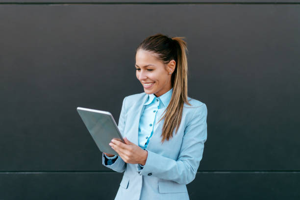 istock Smiling Caucasian woman in suit using tablet outdoors. Dark background. 1081454076