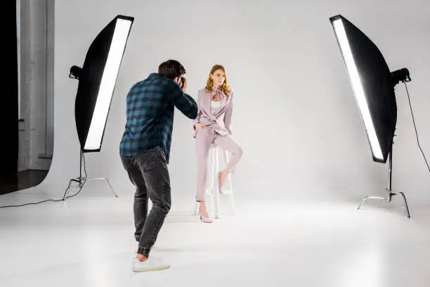 Photo of back view of photographer shooting beautiful young female model in photo studio