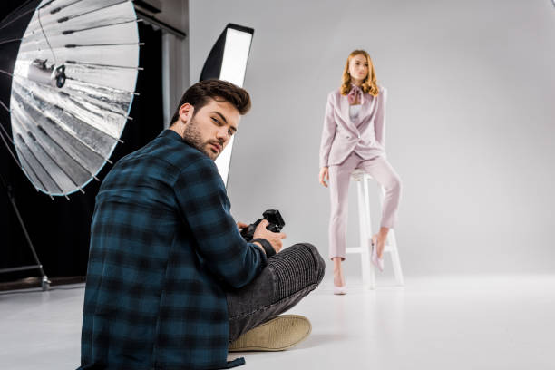 istock photographer sitting and looking at camera while beautiful female model posing in studio 1081475958