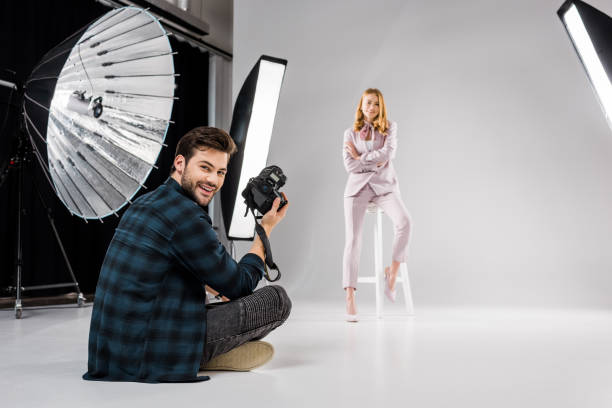 istock photographer sitting and smiling at camera while beautiful female model posing in studio 1081475964