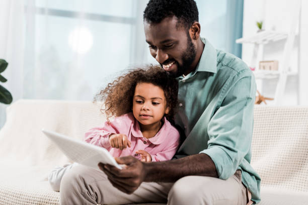 istock handsome african american father and daughter using digital tablet while sitting on couch 1081478958