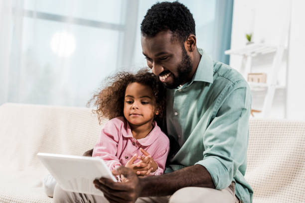 istock smiling african american father and kid using digital tablet while sitting on couch 1081478968