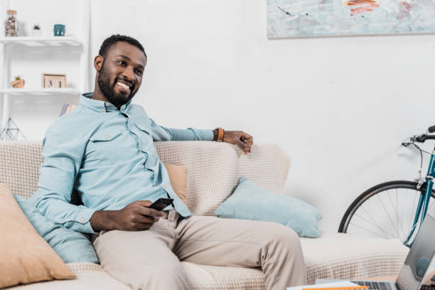 istock happy african american man sitting on couch with remote controller 1081480320