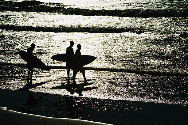 Sylwetka trzech surferów na plaży o zachodzie słońca – zdjęcie