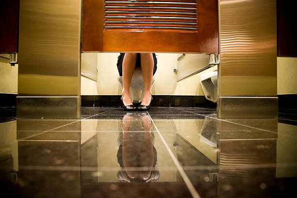 Woman Sitting on Toilet Female woman shown sitting on a toilet seat in a public washroom. Reflection of female is shown on the floor. Woman wearing business attire and wearing highheels.  Feet are pointing towards eachother. public restroom stock pictures, royalty-free photos & images