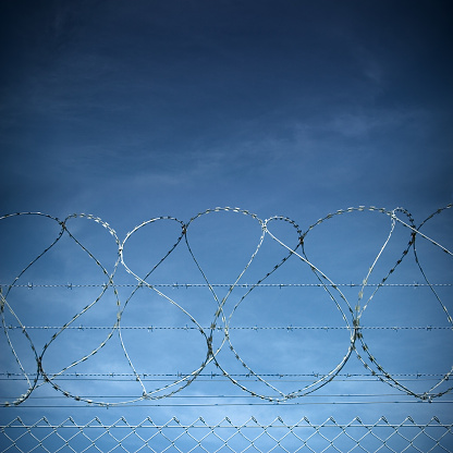 Barbwire as used for military bases or prisons against a deep blue sky.