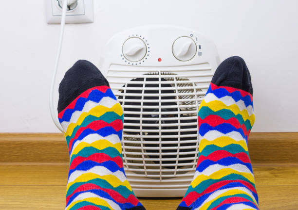 Feet in bright socks near electric fan heater at home. Close-up, selective focus. Feet in bright socks near electric fan heater at home. Close-up, selective focus. electric heater photos stock pictures, royalty-free photos & images