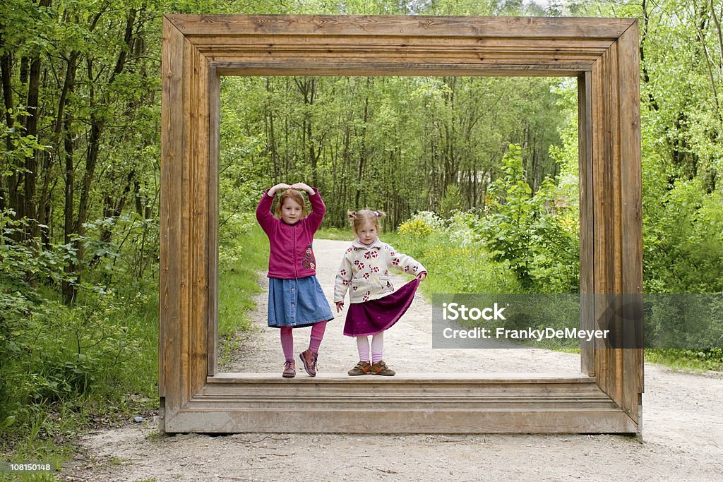 Due ragazzine in piedi con cornice di legno nella foresta - Foto stock royalty-free di Cornice per foto