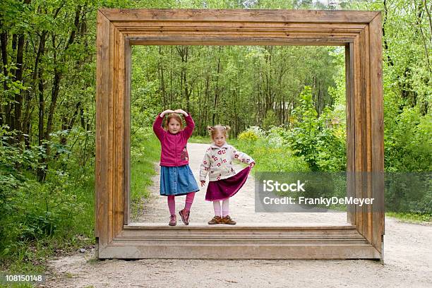 Due Ragazzine In Piedi Con Cornice Di Legno Nella Foresta - Fotografie stock e altre immagini di Cornice per foto