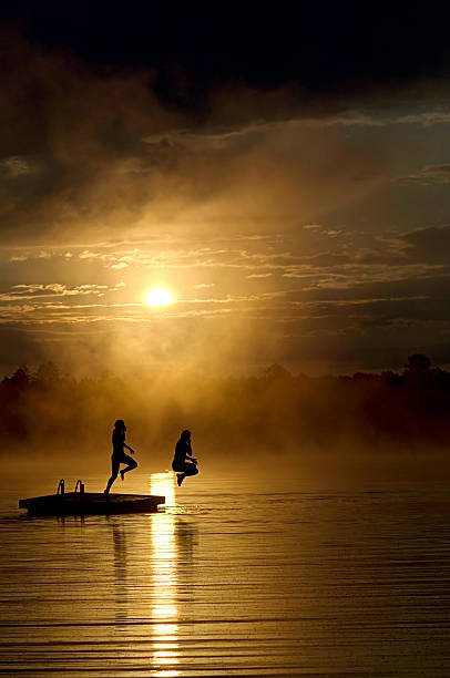 istock Silhouette of Poeple Jumping off Dock at Sunset 108150236