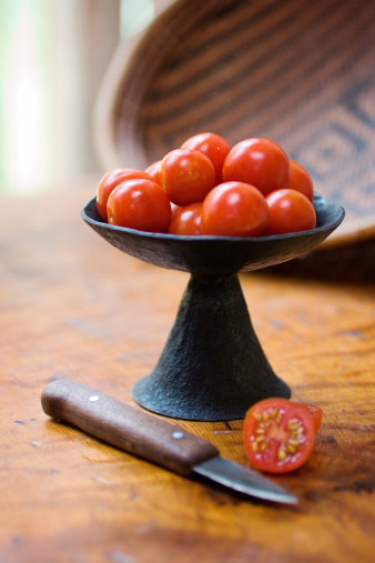 A studio photo of fresh ripe cherry tomatoes in a white bowl with one tomato on the side..