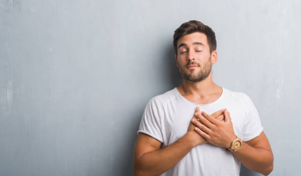 istock Handsome young man over grey grunge wall smiling with hands on chest with closed eyes and grateful gesture on face. Health concept. 1081504112