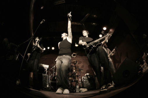 Band playing on a stage. Male guitarist, male bassist and female drummer. Shot with strobes and slow shutter speed to create lighting atmosphere and blur effects. Slight motion blur on performers.