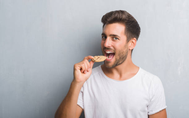 istock Handsome young man over grey grunge wall eating chocolate chip cooky with a confident expression on smart face thinking serious 1081504596