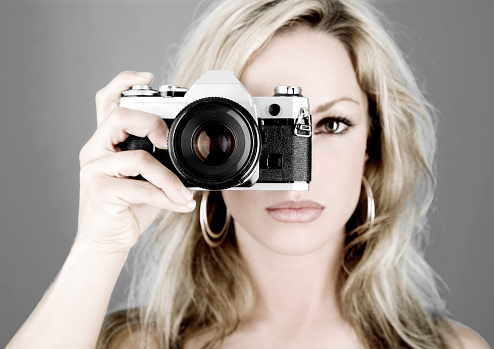 Woman holding up a camera about to take a photo. Image has been colorized.