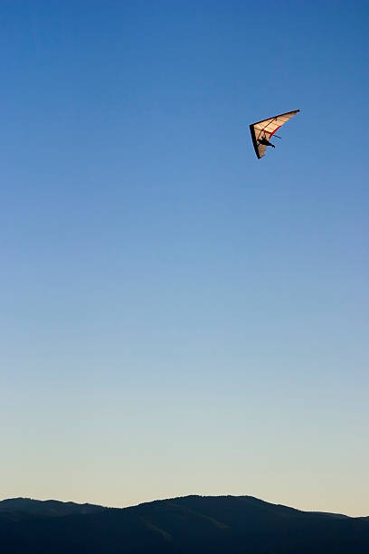 A vintage aircraft soars over a tranquil countryside landscape at golden hour with clear skies and rolling fields.