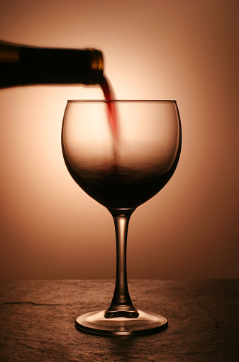 A closeup of red wine being poured in a wine glass against a white background.