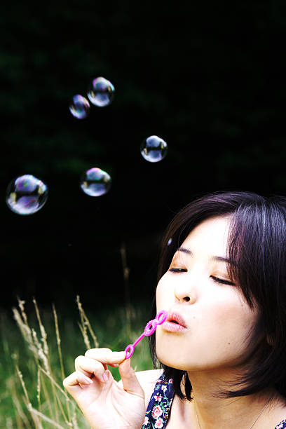 istock Young Asian Woman Blowing Bubbles in Field 108151237