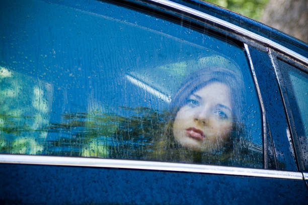 Young woman longingly looks out the window of a car during a rain storm.
