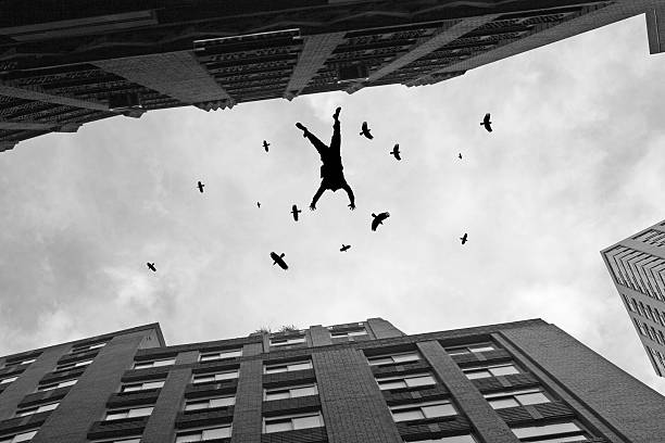 Businessman Falling Off Office Building Roof with Birds Flying stock photo