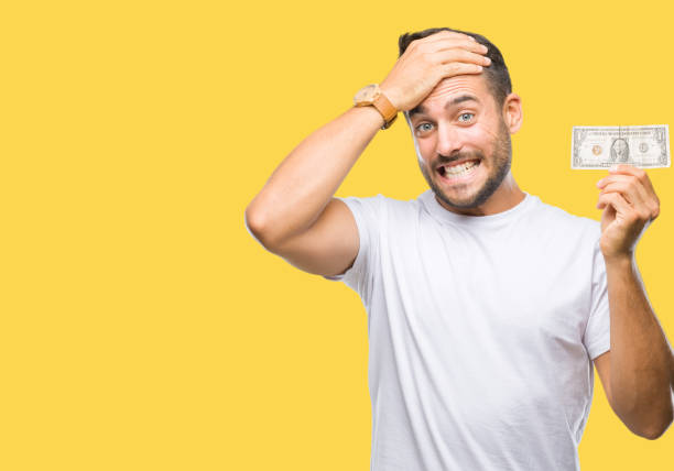 istock Young handsome man holding dollars over isolated background stressed with hand on head, shocked with shame and surprise face, angry and frustrated. Fear and upset for mistake. 1081515354