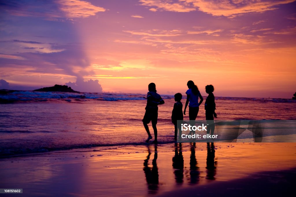 Silhouette di quattro bambini sulla spiaggia al tramonto - Foto stock royalty-free di Abbigliamento casual