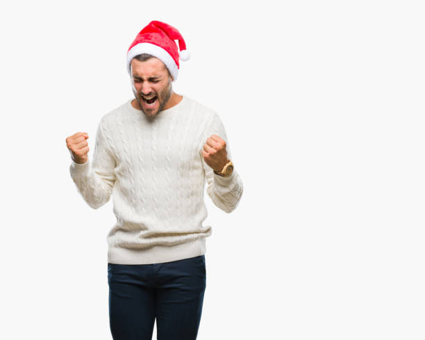 jeune bel homme portant chapeau de père noël sur fond isolé très heureux et excité faisant le geste de vainqueur avec les bras levés, sourire et criant pour le succès. notion de célébration. - men sweater excitement satisfaction photos et images de collection