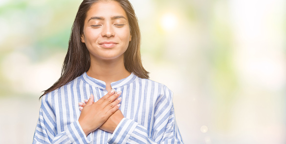 Young beautiful arab woman over isolated background smiling with hands on chest with closed eyes and grateful gesture on face. Health concept.