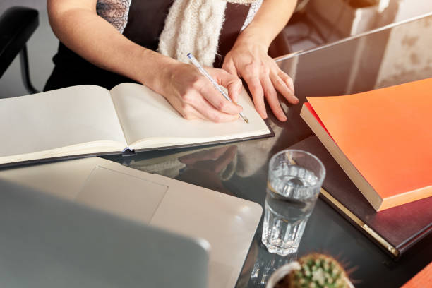 istock Woman's hands making notes on white spread notebook. Cactus and glass of water. Young woman or student working and writing on paper, space for text. 1081521208