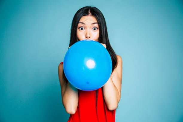 istock Happy woman in red is blowing a blue balloon in studio 1081532806