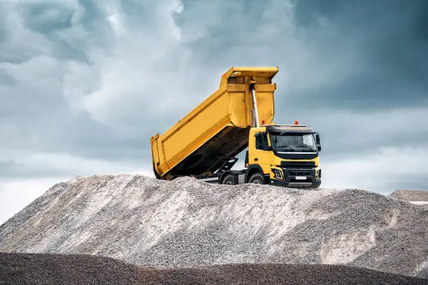 Delivery of sand to the construction site by yellow truck with raised body