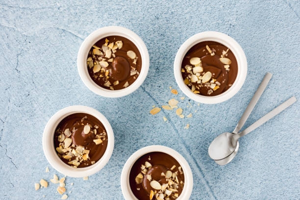 Chocolate Pudding in Ramekins and Teaspoons on Blue Homemade chocolate pudding in three white ceramic ramekins with roasted almond slivers and teaspoons on light blue concrete background. Top view. almond slivers stock pictures, royalty-free photos & images