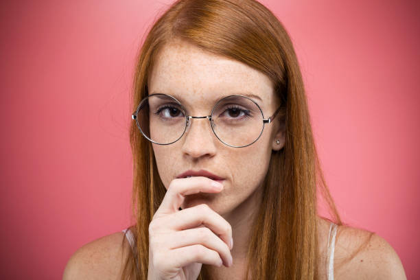 istock Interesting young woman with eyeglasses thinking and looking at camera over pink backgound. 1081565810