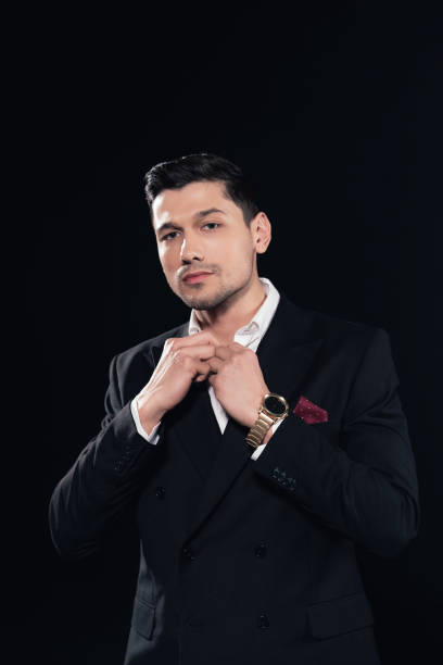 istock handsome man in suit looking at camera and buttoning up shirt isolated on black 1081577816