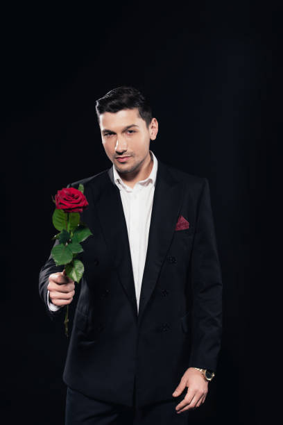 istock man in suit looking at camera and holding red rose isolated on black 1081577820