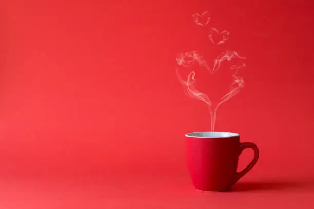 Photo of Cup of tea or coffee with steam in one heart shape on red background. Valentine's day celebration or love concept. Copy space