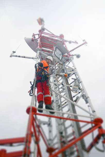 Handsome rope access technician climbing on the tower - antenna with hooks and looking down