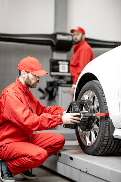 Auto mechanics making wheel alignment at the car service Handsome auto mechanic in red uniform fixing disk for wheel alignment at the car service wheel cap stock pictures, royalty-free photos & images