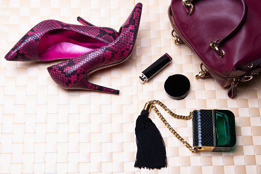 Top view to flat lay fashionable high heels, leather handbag, perfume and cosmetics on a bright table cloth.