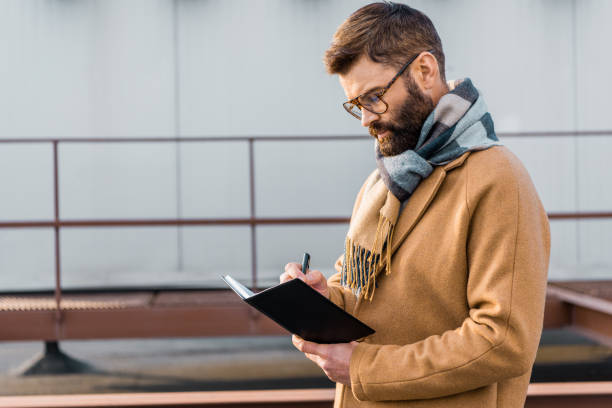 istock Focused businessman standing in coat and writing in notebook 1081598844