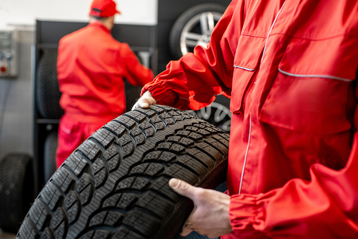 Worker in uniform carrying new tires at the car service or store, close-up view