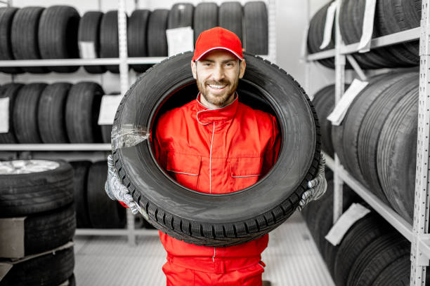 Worker wearing car tire in the storage Funny portrait of a smiling worker in red uniform wearing car tire on his head in the warehouse tire vehicle part stock pictures, royalty-free photos & images