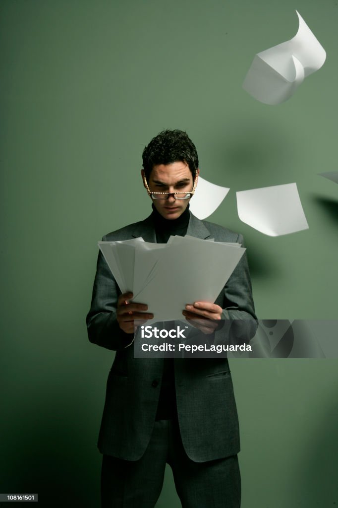 Empresario leyendo periódicos con papel volando alrededor de él - Foto de stock de A la moda libre de derechos
